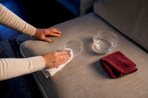 Hands treating a water stain on couch fabric